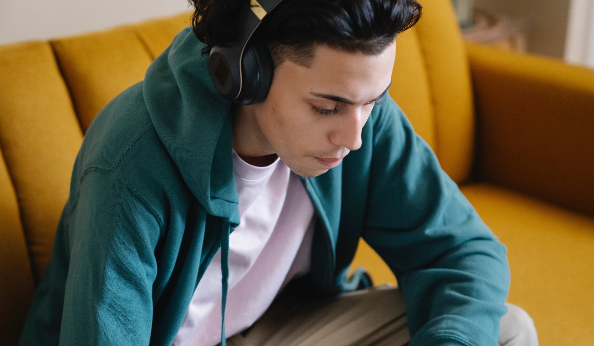 teanage man on a yellow couch listening to over-ear headphones and wearing a green hoodie